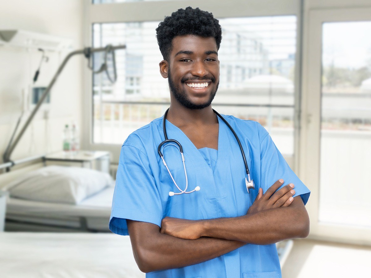 Smiling BSN student in scrubs standing in a hospital room, representing Bachelor of Science in Nursing programs in Arkansas.