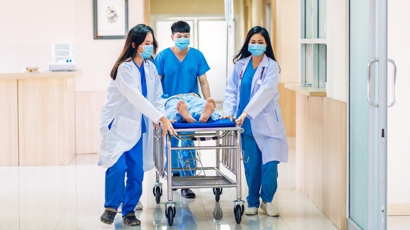 Medical team in scrubs and lab coats, including a paramedic pushing a patient on a gurney through a hospital hallway, representing hands-on training in a paramedic to RN bridge program
