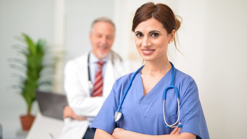 Nurse in blue scrubs with her arms crossed and another doctor in the background