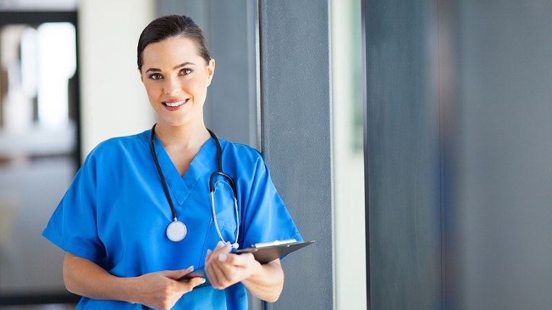 Nurse practitioner student enrolled in a no GRE NP program, standing in a hallway with a tablet.