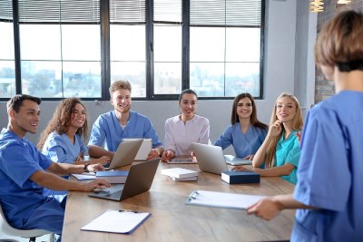 Nursing students in Texas participate in a collaborative nurse educator training session, gathered around a table with laptops and notes in a classroom setting.