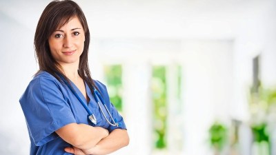 Confident nurse in blue scrubs standing with arms crossed, representing the best neonatal nurse practitioner programs in Colorado.