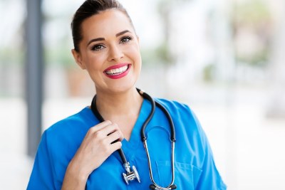 Nursing student in blue scrubs smiling outside a Kansas healthcare facility.