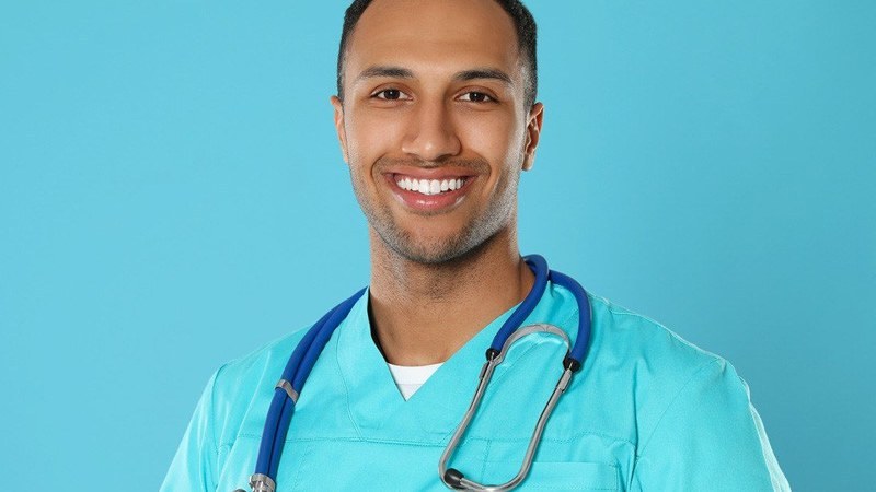 Nursing student wearing scrubs and a stethoscope, smiling while enrolled in the fastest NP program.