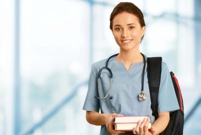 Nursing student in Austin wearing scrubs with books and a backpack inside a medical facility.