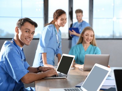 Nursing students in Minnesota ADN programs studying together in a classroom with laptops and clinical uniforms.