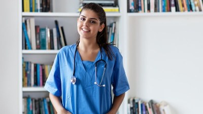 Neonatal Nurse Practitioner student in scrubs standing in front of bookshelves while preparing for neonatal care training.