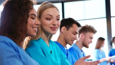 Group of medical assistant students in scrubs seated in a classroom setting in New York, engaged in hands-on training with digital tablets and lab materials.