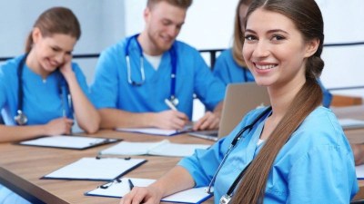 Nursing students in blue scrubs taking notes in a classroom at a nursing school in Atlanta.