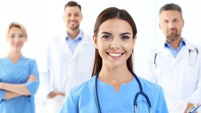 Nurses in an ACNP program standing together in a clinical setting, with one nurse in the foreground smiling confidently.