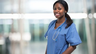 Smiling nurse in scrubs with a stethoscope, currently enrolled in a dual FNP/PMHNP program.