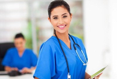 Smiling nursing student in scrubs holding a tablet at a nursing school classroom in Miami, Florida