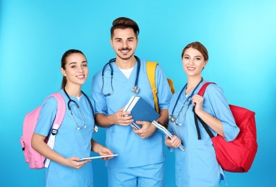 Three nursing students in scrubs with backpacks and notebooks, standing in front of a blue background, representing DNP programs in Florida.