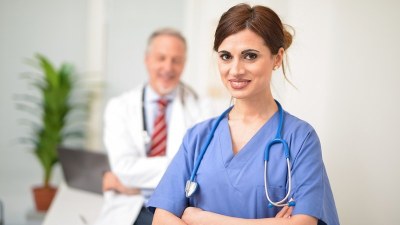 Nurse in blue scrubs with her arms crossed and another doctor in the background