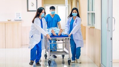 Medical team in scrubs and lab coats, including a paramedic pushing a patient on a gurney through a hospital hallway, representing hands-on training in a paramedic to RN bridge program
